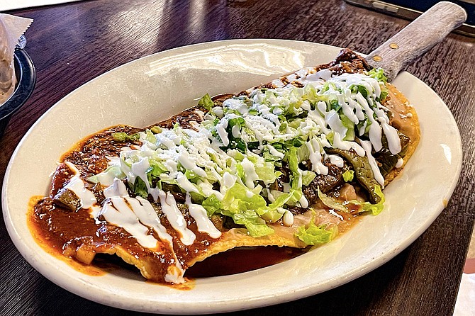 The somewhat football shaped Entomatado huarache, topped with refried beans, lettuce, crema, pork, and two salsas
