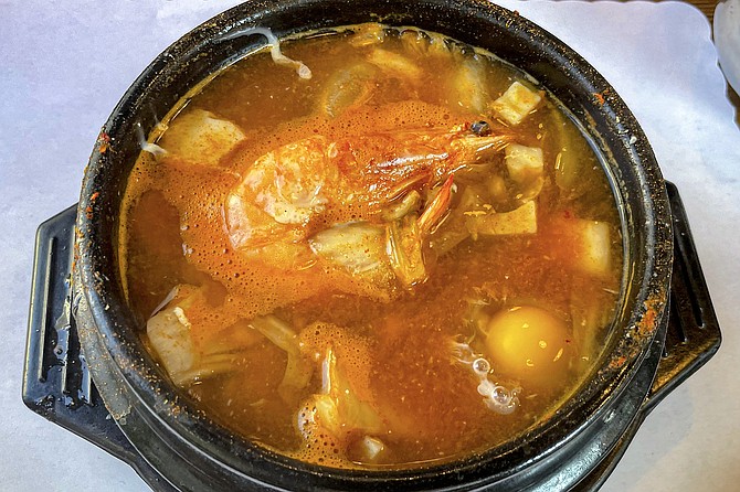 A shrimp is visible beneath the surface of the broth in the chef's special soft tofu stew.
