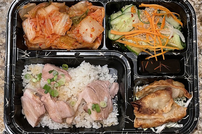 A pork belly bento box with cucumber salad, kimchi, and beef gyoza