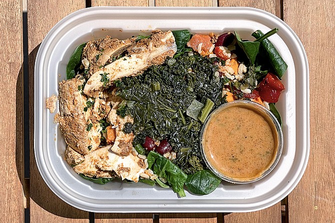 A packaged meal of creole chicken, sausage, sweet potatoes, and kale