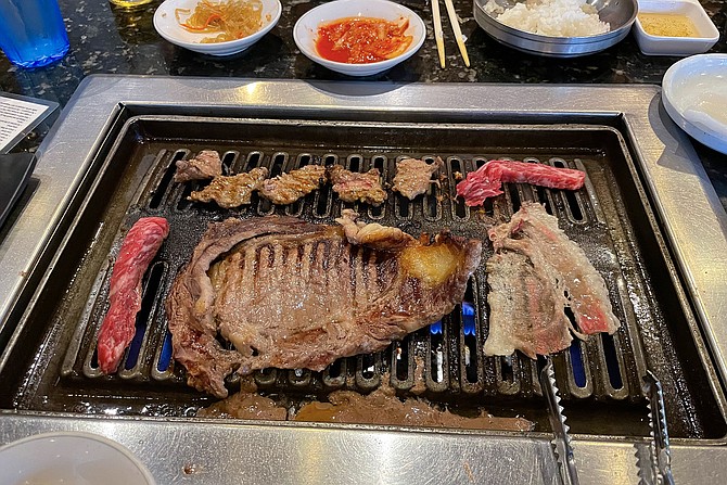 Several kinds of beef — including a thin ribeye steak — cooking on a table grill