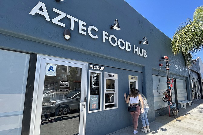 Aztec Food Hub is a collection of virtual kitchens, behind windows facing a college area sidewalk.