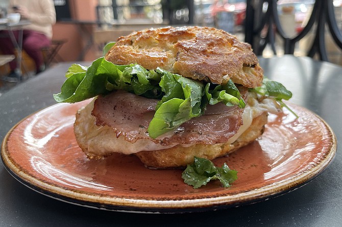 A breakfast sandwich of fried egg, arugula, and ham, made on a gougére roll