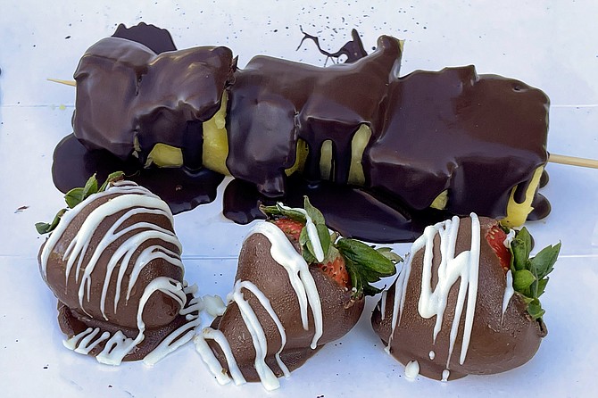 A skewer of pineapple chunks dipped in dark chocolate, and strawberries dipped in milk chocolate, with white chocolate drizzle