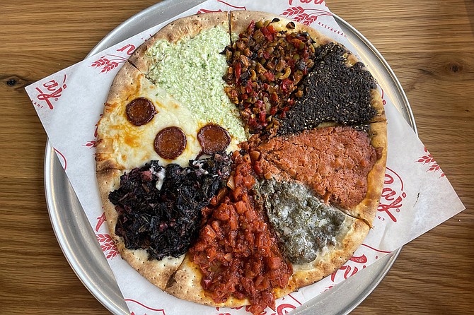 The cocktail mana'ish, a Lebanese-style flatbread featuring eight different sets of toppings. Clockwise from the top: olives mix, za'atar spice blend, keshik, kafta, spicy tomatoes, spinach and sumac, soujouk and cheese, parsley and cheese.