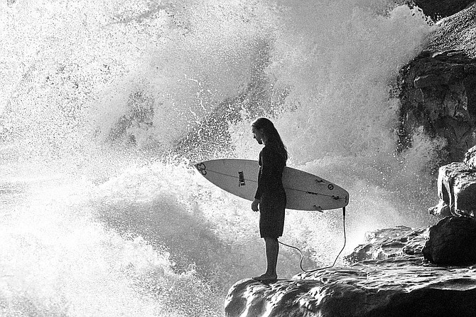 A surfer waits on the rocks for break in a large set of waves.