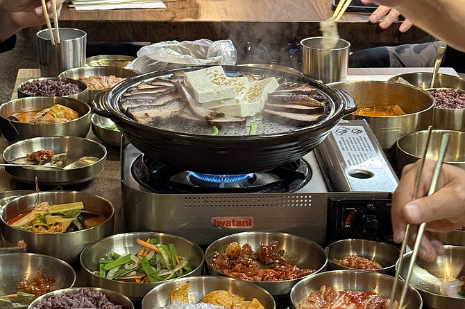 A large party shares bossam and tofu straight from a tabletop grill