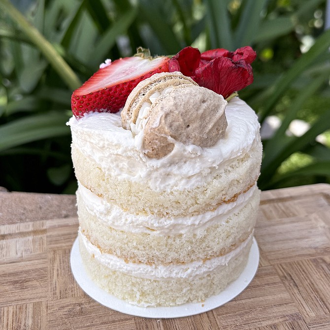 A three layer white cake with Berries, flower, and macaron