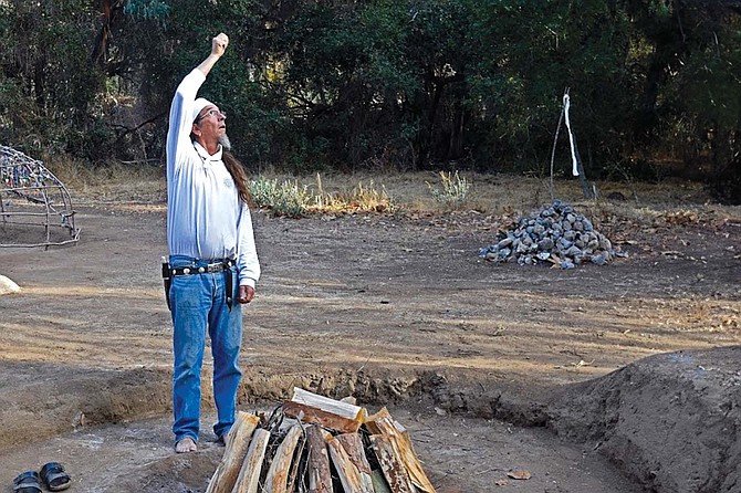 Hand raised to the sky and bare feet on the ground, Shaman Goodknife blesses the fire.