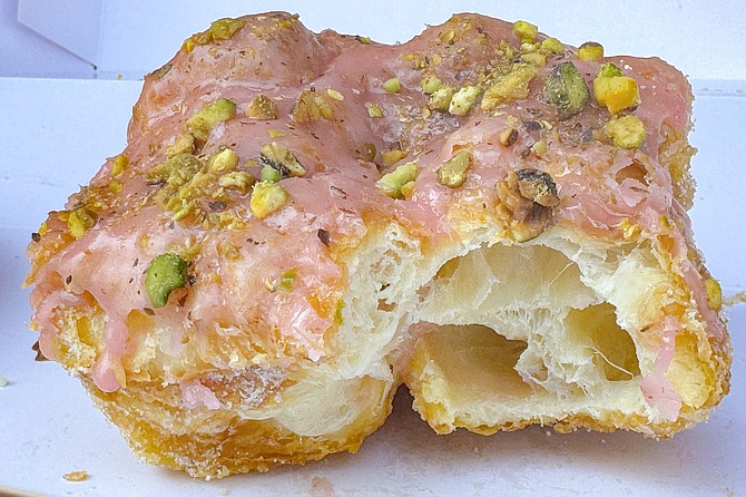 A raspberry pistachio donut, with a bite revealing its croissant-like interior