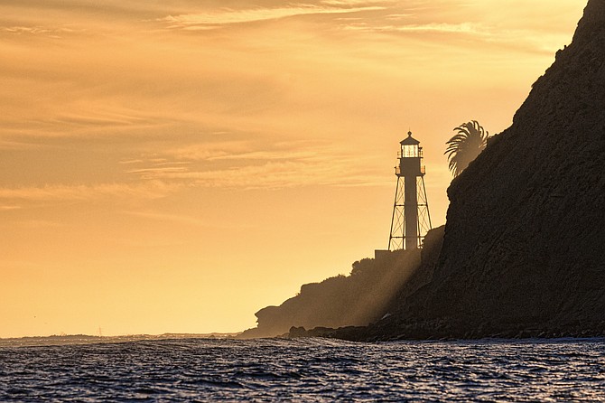 A sunset behind the Point Loma peninsula lights up the lighthouse.