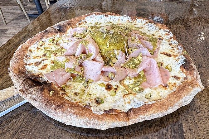 A pizza topped by mortadella, a ball of burrata cheese, and pistachio pesto