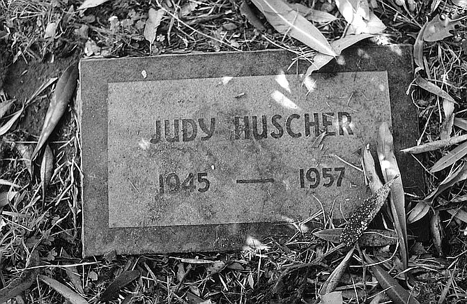Judy’s stone, which says simply “Judy Huscher, 1945–1957,” sits between Hank Decking and an oleander tree, whose long, poisonous leaves make flickering shadows on her name.