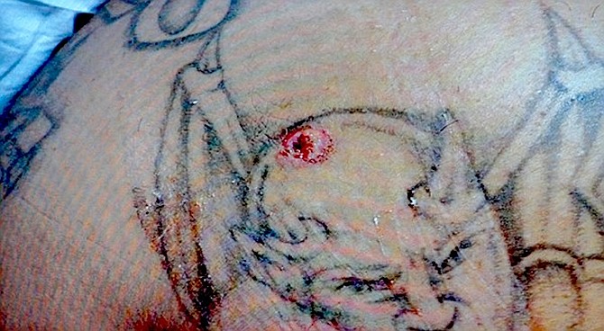 Bullet hole in tattoo of Satan’s head, on Nico’s back shoulder